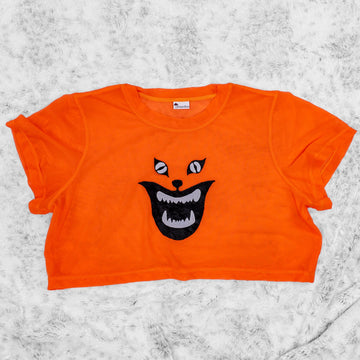 A flat lay image showcasing a bright orange stretch mesh crop top tee shirt with short sleeves a round neckline. The top is adorned with an intricate Demon Cat appliqué from cult film Hausu(1977) for a touch of vintage horror. The background is neutral, highlighting the top's details and textures.