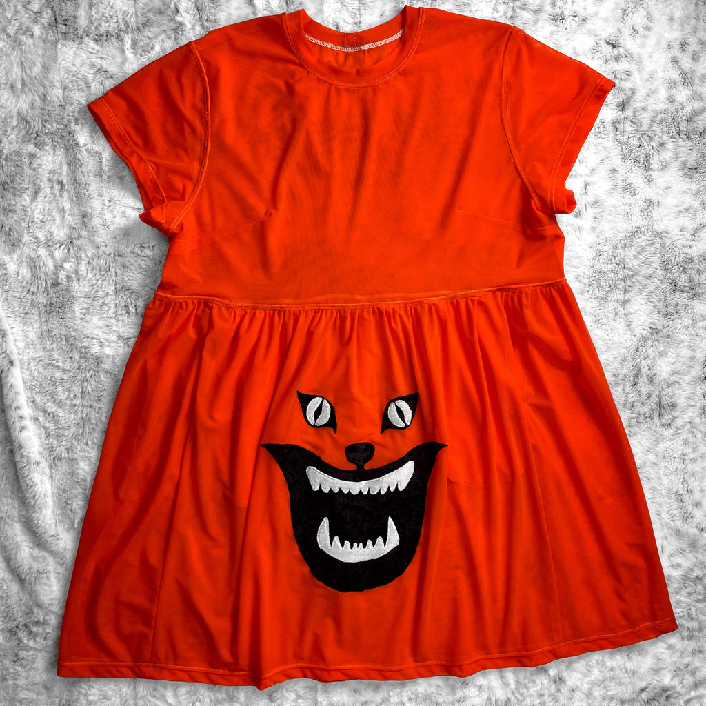 A flat lay image showcasing a bright orange stretch mesh babydoll dress with short sleeves adorned with an intricate Demon Cat appliqué from cult film Hausu(1977) for a touch of vintage horror. The background is neutral, highlighting the dress's details and textures.