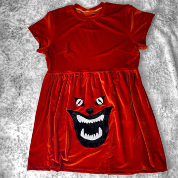 A flat lay image showcasing a rusty orange velvet babydoll dress with short sleeves adorned with an intricate Demon Cat appliqué from cult film Hausu (1977) for a touch of vintage horror. The dress features soft, luxurious fabric in rich colors. The background is neutral, highlighting the dress's details and textures.