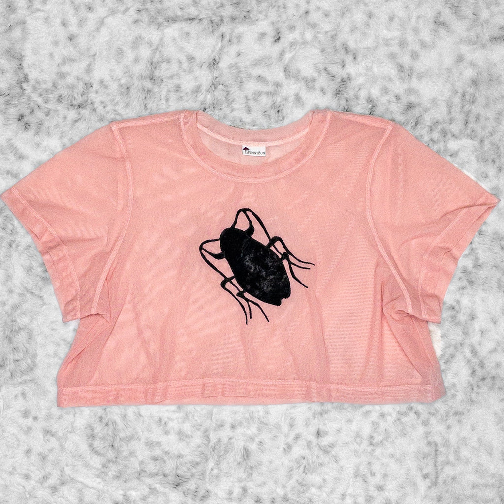 A flat lay image showcasing a blush pink stretch mesh crop top tee shirt with short sleeves a round neckline. The top is adorned with an intricate roach appliqué inspired by cult film Hairspray (1988) from the Pope of Trash himself. The background is neutral, highlighting the top's details and textures.