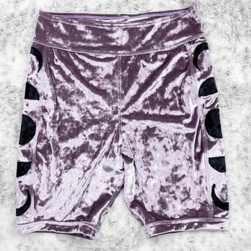 A flat lay image showcasing purple haze crushed velvet bike shorts with moon phase appliqué along the side seams, showcasing a stylish and unique design. The shorts feature soft, luxurious fabric in an icy cool pastel. The background is neutral, highlighting the shorts' details and textures.