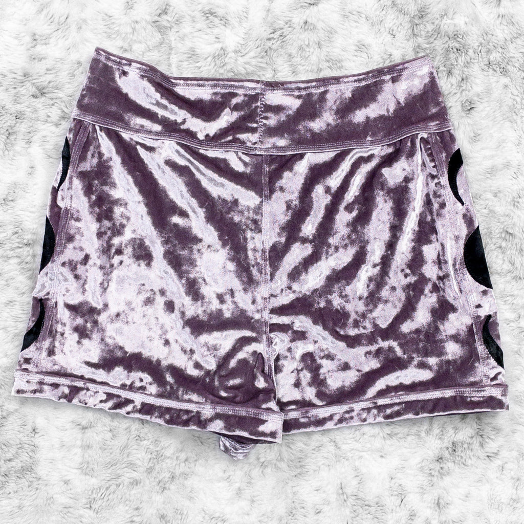 A flat lay image showcasing the back of a purple haze crushed velvet booty shorts with moon phase appliqué along the side seams. The shorts feature soft, luxurious fabric in an icy cool pastel. The background is neutral, highlighting the shorts' details and textures.