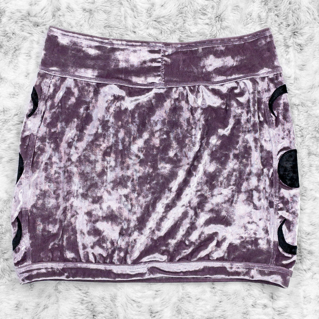 A flat lay image showcasing the back of a purple haze crushed velvet mini skirt with moon phase appliqué along the side seams. The shorts feature soft, luxurious fabric in an icy cool pastel. The background is neutral, highlighting the shorts' details and textures.