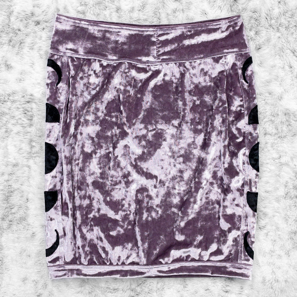 A flat lay image showcasing the back of a purple haze crushed velvet pencil skirt with moon phase appliqué along the side seams. The shorts feature soft, luxurious fabric in an icy cool pastel. The background is neutral, highlighting the shorts' details and textures.