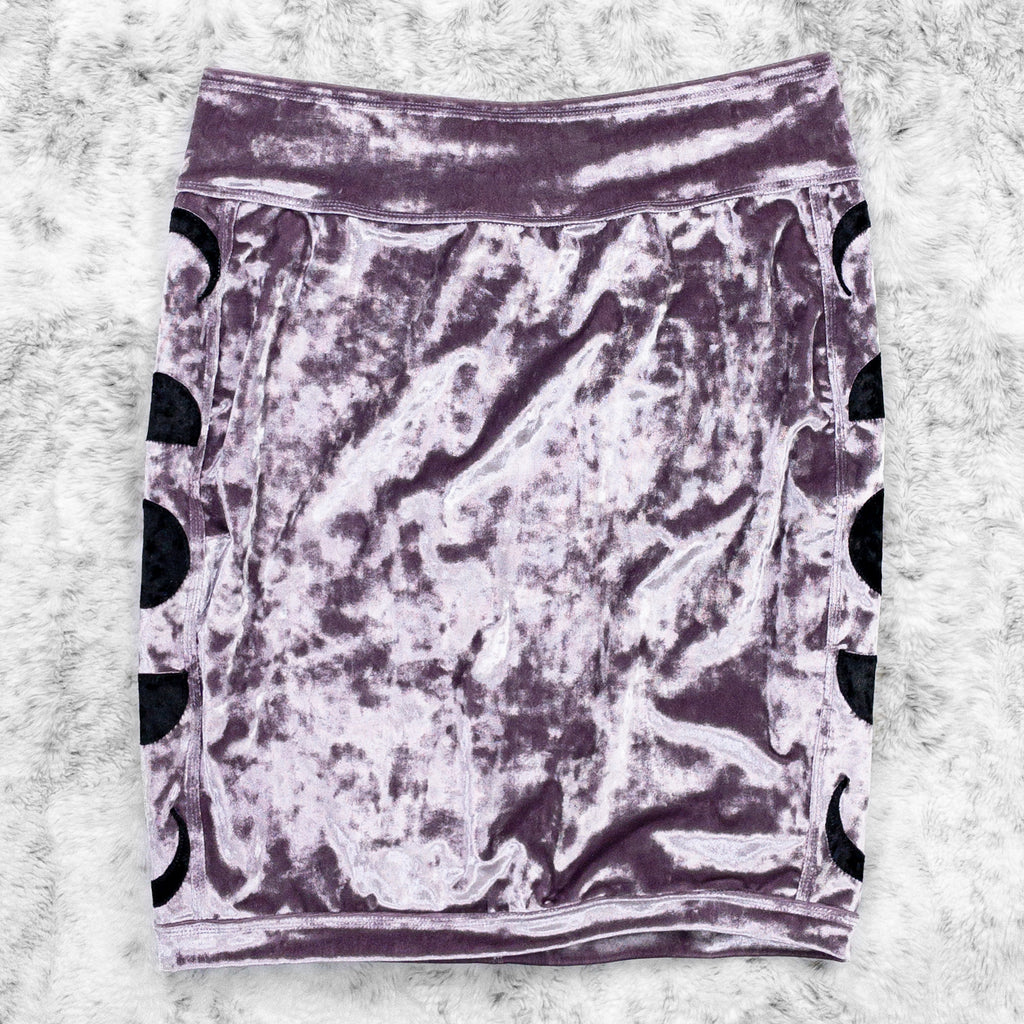 A flat lay image showcasing a purple haze crushed velvet pencil skirt with moon phase appliqué along the side seams, showcasing a stylish and unique design. The shorts feature soft, luxurious fabric in an icy cool pastel. The background is neutral, highlighting the shorts' details and textures.