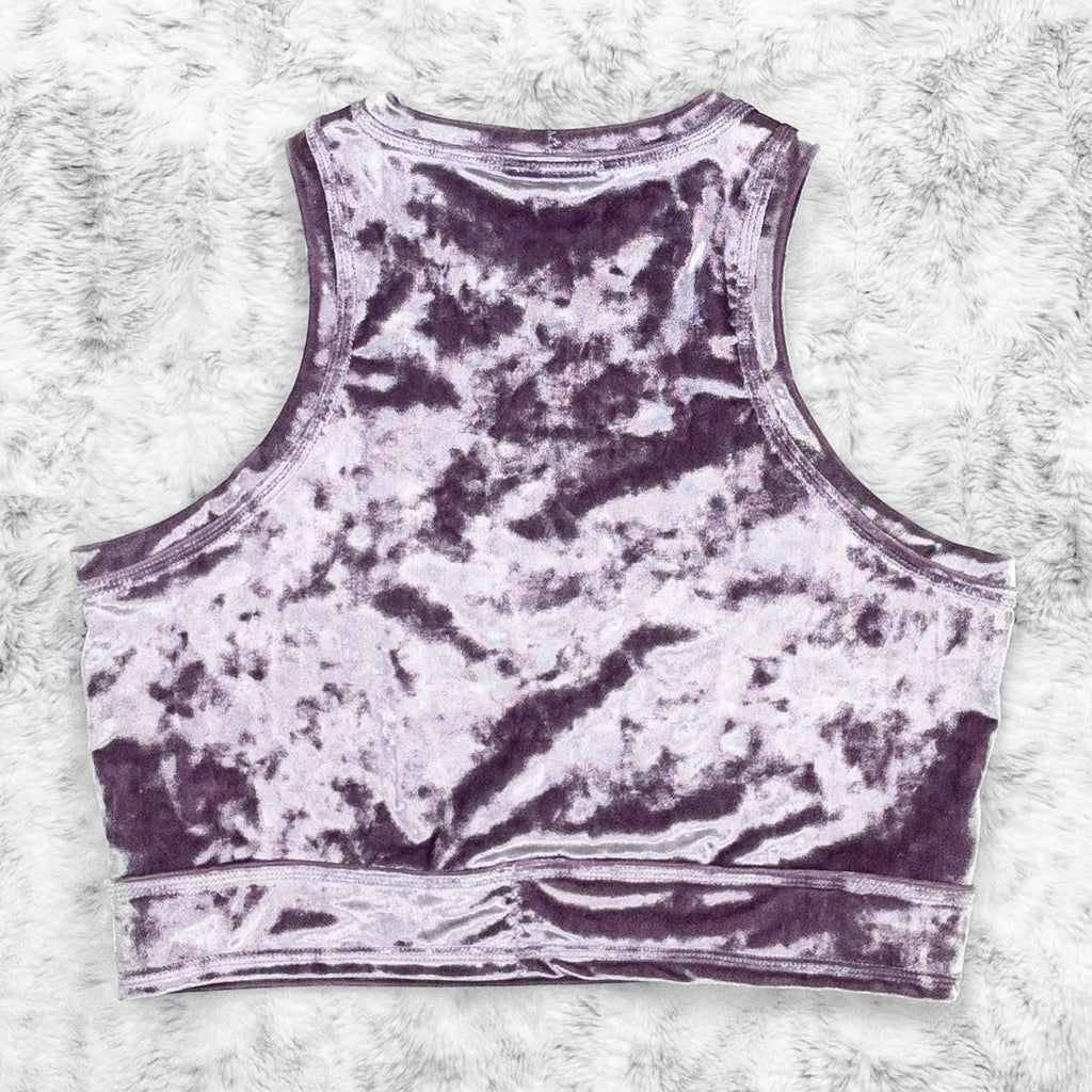 A flat lay image showcasing the back of a purple haze crushed velvet crewneck close cut crop with princess seams and a crescent moon appliqué on the centerfront. The top features soft, luxurious fabric in an icy cool pastel purple. The background is neutral, highlighting the shorts' details and textures.