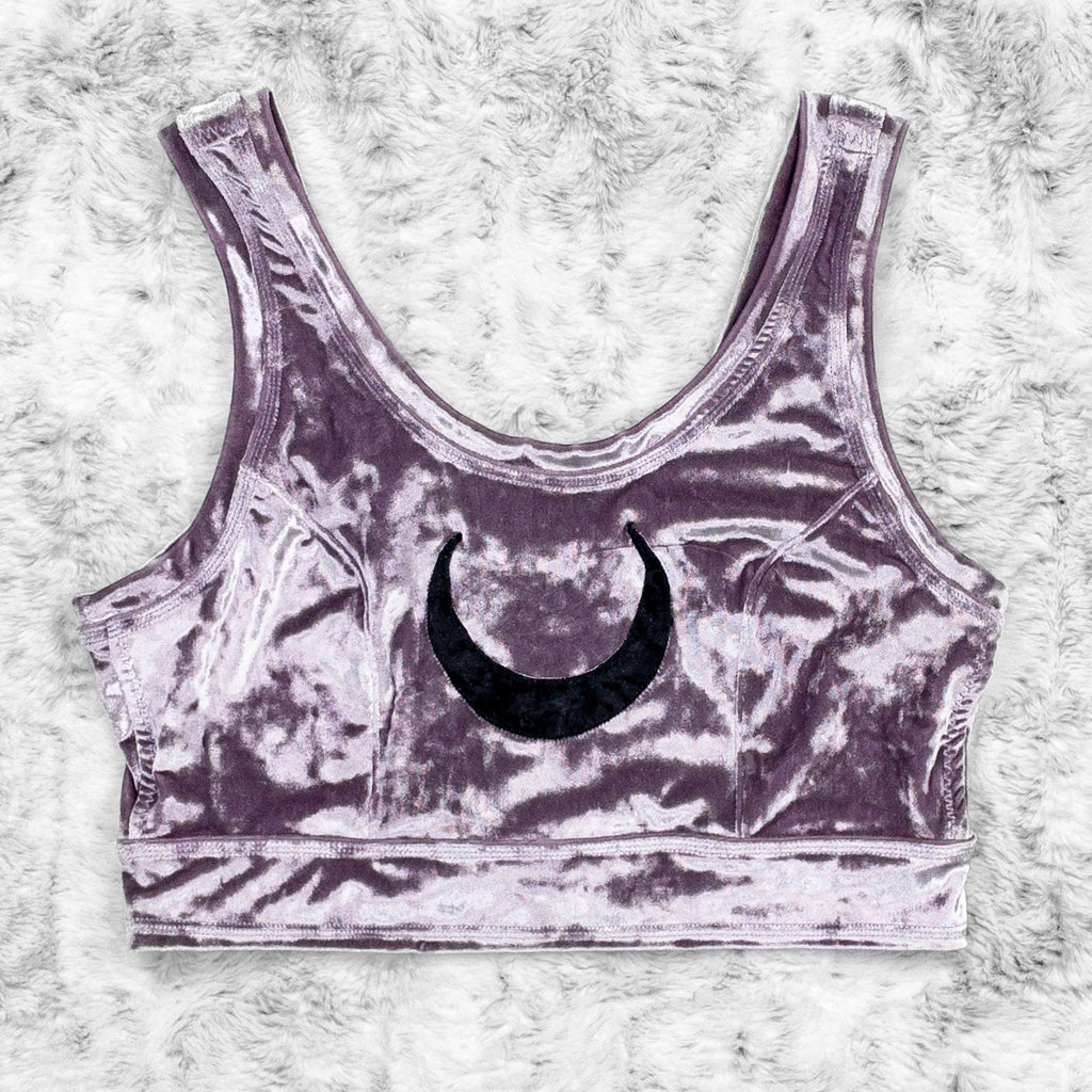 A flat lay image showcasing a purple haze crushed velvet scoopneck close cut crop with princess seams and a crescent moon appliqué on the centerfront, showcasing a stylish and unique design. The shorts feature soft, luxurious fabric in an icy cool pastel. The background is neutral, highlighting the shorts' details and textures.