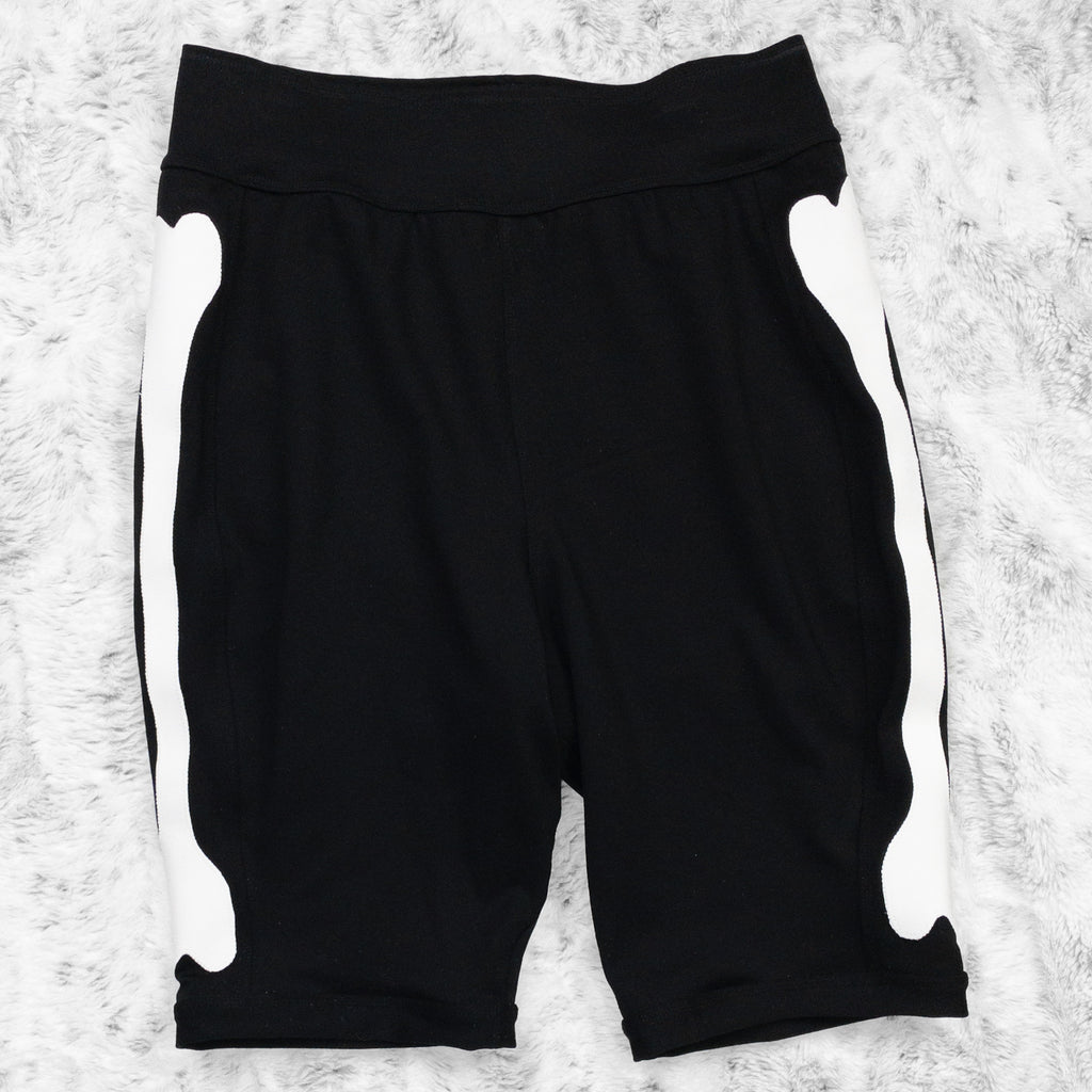 A flat lay image showcasing black 4-way stretch ponte knit bike shorts with femur bone appliqué along the side seams, showcasing a stylish and unique design. The shorts feature soft, luxurious fabric in an inky black. The background is neutral, highlighting the shorts' details and textures.