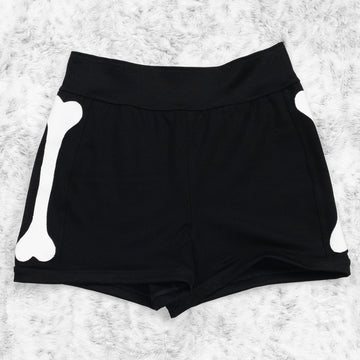 A flat lay image showcasing black 4-way stretch ponte knit bike shorts with femur bone appliqué along the side seams, showcasing a stylish and unique design. The shorts feature soft, luxurious fabric in an inky black. The background is neutral, highlighting the shorts' details and textures.