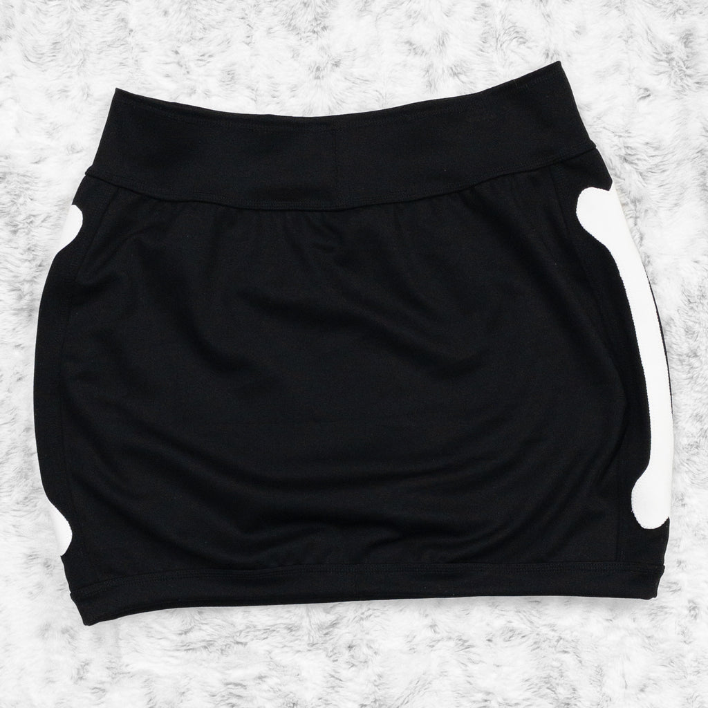 A flat lay image showcasing the back of a black 4-way stretch ponte knit mini skirt with femur bone appliqué along the side seams. The skirt features soft, luxurious fabric in an inky black. The background is neutral, highlighting the skirt's details and textures.