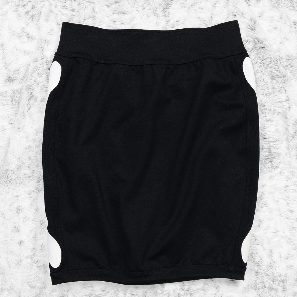 A flat lay image showcasing a black 4-way stretch ponte knit pencil skirt with femur bone appliqué along the side seams, showcasing a stylish and unique design. The skirt features soft, luxurious fabric in an inky black. The background is neutral, highlighting the skirt's details and textures.