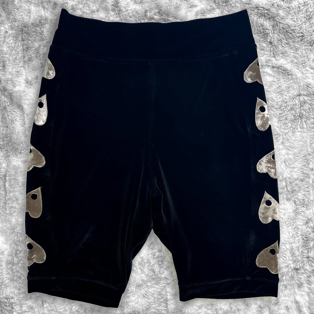 A flat lay image showcasing premium smooth black velvet bike shorts with witchy planchette appliqué along the side seams, showcasing a stylish and unique design. The shorts feature soft, luxurious fabric in an inky black. The background is neutral, highlighting the shorts' details and textures.