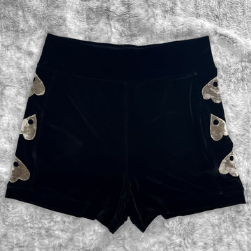 A flat lay image showcasing premium smooth black velvet booty shorts with witchy planchette appliqué along the side seams, showcasing a stylish and unique design. The shorts feature soft, luxurious fabric in an inky black. The background is neutral, highlighting the shorts' details and textures.